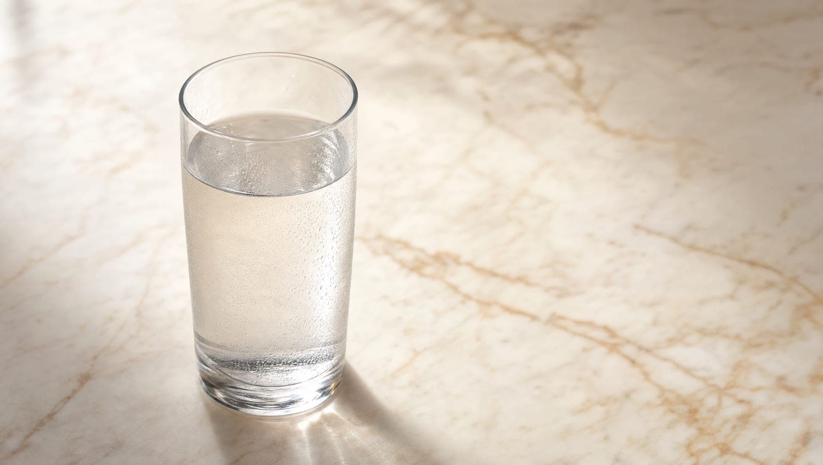 Tall clear glass of water on warm marble surface with veining